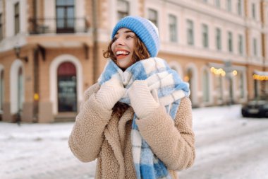 Eşarp ve şapkaya sarılmış mutlu bir kadın güneşli bir günde karlı bir sokakta duruyor. Şık giyinmiş genç bir turist dondurucu havanın tadını çıkarıyor. Yürüme, tarz ve moda kavramı..
