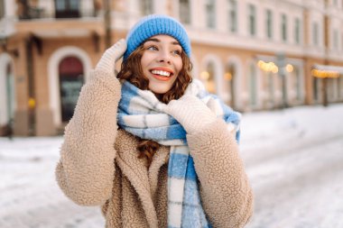 Eşarp ve şapkaya sarılmış mutlu bir kadın güneşli bir günde karlı bir sokakta duruyor. Şık giyinmiş genç bir turist dondurucu havanın tadını çıkarıyor. Yürüme, tarz ve moda kavramı..