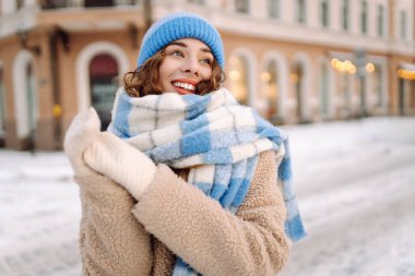 Eşarp ve şapkaya sarılmış mutlu bir kadın güneşli bir günde karlı bir sokakta duruyor. Şık giyinmiş genç bir turist dondurucu havanın tadını çıkarıyor. Yürüme, tarz ve moda kavramı..