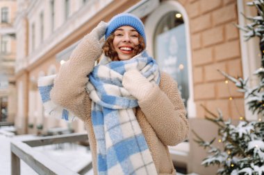 Eşarp ve şapkaya sarılmış mutlu bir kadın güneşli bir günde karlı bir sokakta duruyor. Şık giyinmiş genç bir turist dondurucu havanın tadını çıkarıyor. Yürüme, tarz ve moda kavramı..