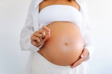 Samimi bir odada ayakta duran hamile bir kadının ek malzemeleri ya da hapları elinde tutması. Çocuk bekleyen güzel bir kadın takviye alır ve göbeğine dokunur. Sağlık kavramları, beklentiler.