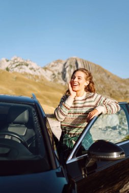 Güneşli bir günde bir dağ yamacında bir kadın yolcu arabanın yanında duruyor. Mutlu kadın dağ manzarasından zevk alır, bir yolculuğun özgürlüğünü hisseder. Yürüyüş kavramı, özgürlük..