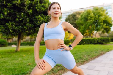 Formda bir kadın güneşli bir parkta esniyor. Aktif giyimli güzel bir kadın güneşte egzersiz yapıyor. Spor anlayışı, eğlence. Etkin yaşam biçimi.