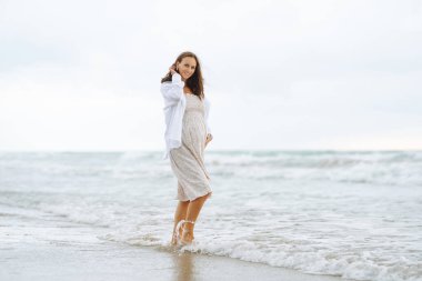 Sevimli bir elbise içinde neşeli bir anne gün batımında kumsalda geziniyor. Hamile kadın deniz manzarasından zevk alır ve özgür hisseder. Fikir: yürüme, rahatlama ve beklenti. Yaşam biçimi.