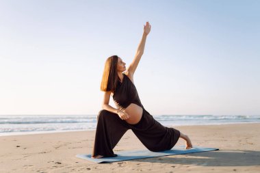 Hamile bir kadın gün batımında denizin kenarındaki yoga minderine uzanır. Bir çocuk bekleyen güzel bir kadın dışarıda meditasyon yapıyor ya da deniz manzarasının tadını çıkarıyor. Konsept rahatlama ve dinlenme..