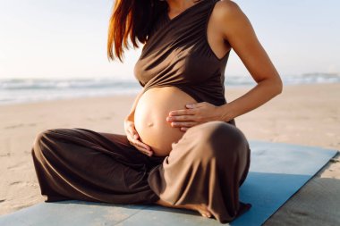 Hamile bir kadın gün batımında denizin kenarındaki yoga minderine uzanır. Bir çocuk bekleyen güzel bir kadın dışarıda meditasyon yapıyor ya da deniz manzarasının tadını çıkarıyor. Konsept rahatlama ve dinlenme..