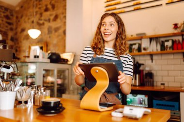 Dişi bir barista, sıcak bir kafede taze demlenmiş kahveyle tezgahın arkasında duruyor. Gülümseyen bir kadın içeride sıcak içecek hazırlar ve servis eder. Konsept rahat, içkiler ve küçük işletmeler..
