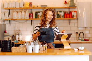 Dişi bir barista, sıcak bir kafede taze demlenmiş kahveyle tezgahın arkasında duruyor. Gülümseyen bir kadın içeride sıcak içecek hazırlar ve servis eder. Konsept rahat, içkiler ve küçük işletmeler..