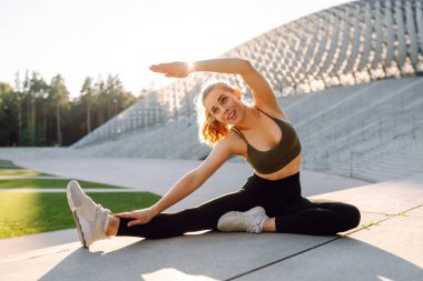 Atletik bir kadın gün batımında dışarıda egzersiz yapar. Spor elbiseli genç bir kadın merdivenli bir platformda egzersiz yapıyor. Spor anlayışı, eğlence. Etkin yaşam biçimi.