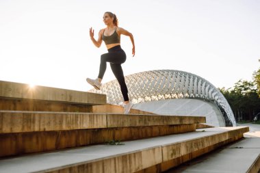 Atletik bir kadın gün batımında dışarıda egzersiz yapar. Spor elbiseli genç bir kadın merdivenli bir platformda egzersiz yapıyor. Spor anlayışı, eğlence. Etkin yaşam biçimi.