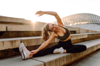 Atletik bir kadın gün batımında dışarıda egzersiz yapar. Spor elbiseli genç bir kadın merdivenli bir platformda egzersiz yapıyor. Spor anlayışı, eğlence. Etkin yaşam biçimi.