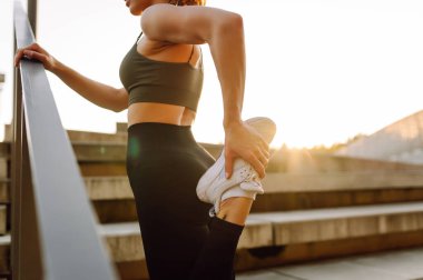 Atletik bir kadın gün batımında dışarıda egzersiz yapar. Spor elbiseli genç bir kadın merdivenli bir platformda egzersiz yapıyor. Spor anlayışı, eğlence. Etkin yaşam biçimi.