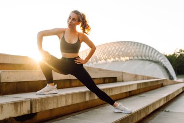 Atletik bir kadın gün batımında dışarıda egzersiz yapar. Spor elbiseli genç bir kadın merdivenli bir platformda egzersiz yapıyor. Spor anlayışı, eğlence. Etkin yaşam biçimi.
