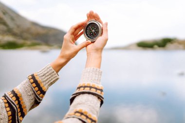 Sırt çantası ve pusula taşıyan kadın yürüyüşçünün arka plandaki kayalık patikada görüntüsü. Yürüyüşçü varış noktasını arar ve güneşli bir günde dağ manzarasının tadını çıkarır. Doğa kavramları, navigasyon.