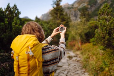 Sırt çantası ve pusula taşıyan kadın yürüyüşçünün arka plandaki kayalık patikada görüntüsü. Yürüyüşçü varış noktasını arar ve güneşli bir günde dağ manzarasının tadını çıkarır. Doğa kavramları, navigasyon.