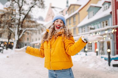 Parlak günlük giysiler içinde mutlu bir turist büyüleyici bir kış kasabasında karla eğleniyor. Güzel bir kadın karlı bir kasabada gezmekten zevk alır. Mevsimlik, kentsellik ve turizm kavramları.