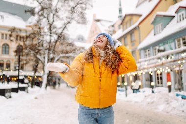 Parlak günlük giysiler içinde mutlu bir turist büyüleyici bir kış kasabasında karla eğleniyor. Güzel bir kadın karlı bir kasabada gezmekten zevk alır. Mevsimlik, kentsellik ve turizm kavramları.