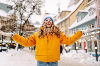 Parlak günlük giysiler içinde mutlu bir turist büyüleyici bir kış kasabasında karla eğleniyor. Güzel bir kadın karlı bir kasabada gezmekten zevk alır. Mevsimlik, kentsellik ve turizm kavramları.