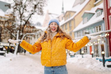 Parlak günlük giysiler içinde mutlu bir turist büyüleyici bir kış kasabasında karla eğleniyor. Güzel bir kadın karlı bir kasabada gezmekten zevk alır. Mevsimlik, kentsellik ve turizm kavramları.