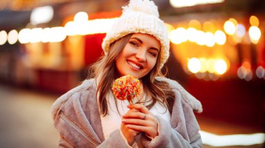 Noel pazarında karamelli elmalı genç bir kadın. Kış kıyafetli gülümseyen kadın poz veriyor..