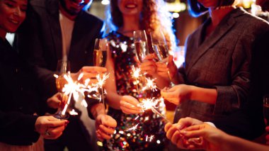 Parıldayan maytaplar ellerinde. Partide arkadaşlarla kış tatilini kutlamak için havai fişek oynuyoruz..