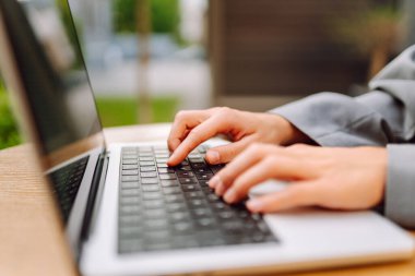 Dışarıdaki masada oturan iş kadınının yakın çekimi. Şık giyinmiş güzel bir kadın terasta güneşli bir günde uzaktan çalışmayı sever. Bağımsızlık, modernlik, tarz ve iş kavramları.