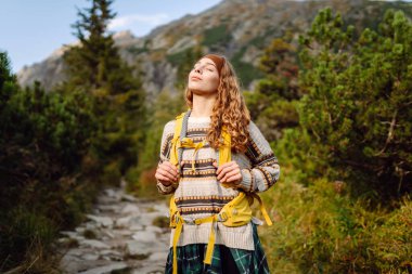 Sırt çantalı bir bayan yürüyüşçü gün batımında bir dağ zeminine karşı duruyor. Mutlu bir kadın yolculuğunda dağların ve kayalıkların tadını çıkarır. Macera, iz ve aktif yaşam tarzı kavramları.