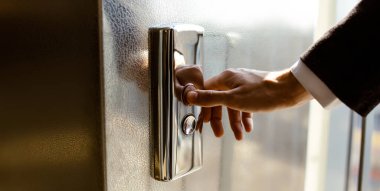 Yakın plan. Bir insan parmağı asansör düğmesine basar. Kapalı mekanda bir erkek eli. Kırmızı bir düğme. Teknoloji kavramı.