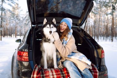 Mutlu bir kadın ve evcil hayvanı bir arabanın bagajında battaniyenin üzerinde oturuyorlar. Sıcak giysiler içindeki genç bir kadın, uzun bir yolculukta ormanda karlı bir günün tadını çıkarıyor. Arkadaşlık kavramı, eğlence, macera.