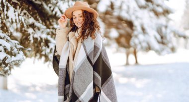 Şık giyinmiş neşeli bir kadın güneşli bir günde karlı bir parkta duruyor. Genç bir kadın karla eğleniyor ve güneşli bir kış gününün tadını çıkarıyor. Doğa ve eğlence kavramı.