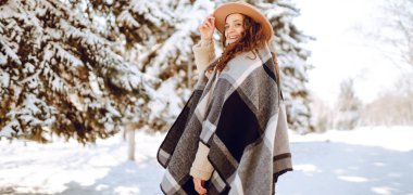 Şık giyinmiş neşeli bir kadın güneşli bir günde karlı bir parkta duruyor. Genç bir kadın karla eğleniyor ve güneşli bir kış gününün tadını çıkarıyor. Doğa ve eğlence kavramı.