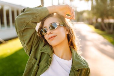 Neşeli bir kadın güneşli bir parkta eğleniyor. Güneş gözlüğü takan bir sırt çantası palmiye ağaçları arasında yürümekten zevk alır. Rahatlama, hafta sonları ve keyif kavramları.