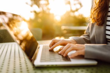 Gün batımında çatı terasında dizüstü bilgisayarda yazı yazan ellerin yakın çekimi. Diz üstü bilgisayarı olan serbest çalışan biri dışarıda çalışıyor. Uzaktan çalışma ve eğitim kavramı.