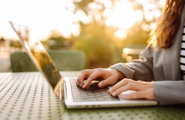 Gün batımında çatı terasında dizüstü bilgisayarda yazı yazan ellerin yakın çekimi. Diz üstü bilgisayarı olan serbest çalışan biri dışarıda çalışıyor. Uzaktan çalışma ve eğitim kavramı.