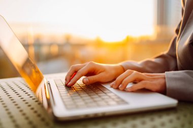 Gün batımında çatı terasında dizüstü bilgisayarda yazı yazan ellerin yakın çekimi. Diz üstü bilgisayarı olan serbest çalışan biri dışarıda çalışıyor. Uzaktan çalışma ve eğitim kavramı.