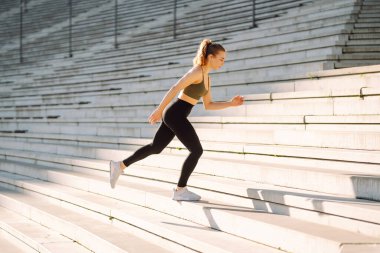 A young woman in sportswear exercises outdoors in the sun. Athlete performs a stretching exercise on special platform. Concept: sports, recreation. Active lifestyle.
