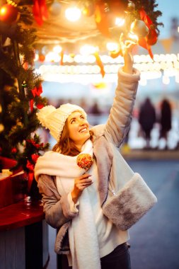 Mutlu bir kadın elinde parlak, büyük bir şekerle markette duruyor. Güzel bir turist Noel pazarının tadını çıkarıyor ve Yeni Yıl atmosferinin tadını çıkarıyor. Tatil, turizm ve tatlı kavramları.