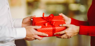 Adam karısına kırmızı kurdeleli bir hediye kutusu veriyor. Sevgililer Günü, tatil ve sürpriz konsept.