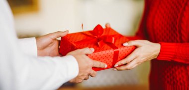 Adam karısına kırmızı kurdeleli bir hediye kutusu veriyor. Sevgililer Günü, tatil ve sürpriz konsept.