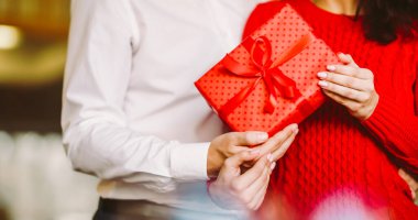 Adam karısına kırmızı kurdeleli bir hediye kutusu veriyor. Sevgililer Günü, tatil ve sürpriz konsept.