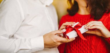 Güneşli bir günde kırmızı bir hediyeyi değiş tokuş eden bir çiftin yakın çekimi. - Sürpriz. Sevgililer Günü. Bir erkek rahat bir ortamda bir kadına hediye verir. Kavramsal olarak, aşk, ilgi ve kutlamayla ilgili..