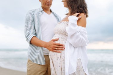 Bekleyen mutlu ebeveynler sahilde durup deniz manzarasının tadını çıkarıyorlar. Bir adam ve hamile karısı deniz kıyısında geziniyorlar. Aile kavramları, beklentiler ve sevgi..