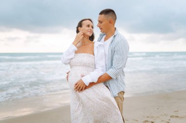 Bekleyen mutlu ebeveynler sahilde durup deniz manzarasının tadını çıkarıyorlar. Bir adam ve hamile karısı deniz kıyısında geziniyorlar. Aile kavramları, beklentiler ve sevgi..