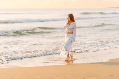 Genç bir kadın deniz kıyısında güneşin doğuşunun tadını çıkarıyor. Mutlu bir kadın kumsalda özgürce dolaşır ve eğlenir. Rahatlama ve zevk kavramı. Yaşam biçimi.