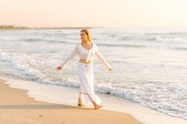 Genç bir kadın deniz kıyısında güneşin doğuşunun tadını çıkarıyor. Mutlu bir kadın kumsalda özgürce dolaşır ve eğlenir. Rahatlama ve zevk kavramı. Yaşam biçimi.