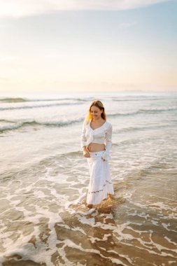 Genç bir kadın deniz kıyısında güneşin doğuşunun tadını çıkarıyor. Mutlu bir kadın kumsalda özgürce dolaşır ve eğlenir. Rahatlama ve zevk kavramı. Yaşam biçimi.