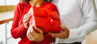 Adam karısına kırmızı kurdeleli bir hediye kutusu veriyor. Sevgililer Günü 'nü kutlayan sevgi dolu bir çift.