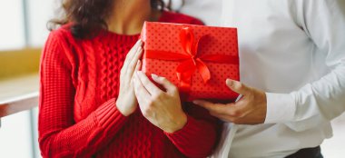 Adam karısına kırmızı kurdeleli bir hediye kutusu veriyor. Sevgililer Günü 'nü kutlayan sevgi dolu bir çift.