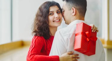 Adam karısına kırmızı kurdeleli bir hediye kutusu veriyor. Sevgililer Günü 'nü kutlayan sevgi dolu bir çift.