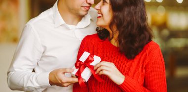 Adam karısına kırmızı kurdeleli bir hediye kutusu veriyor. Sevgililer Günü 'nü kutlayan sevgi dolu bir çift.